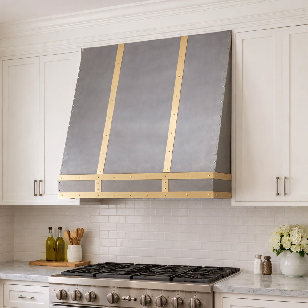 handcrafted stainless steel range hood installed between cream cabinets
